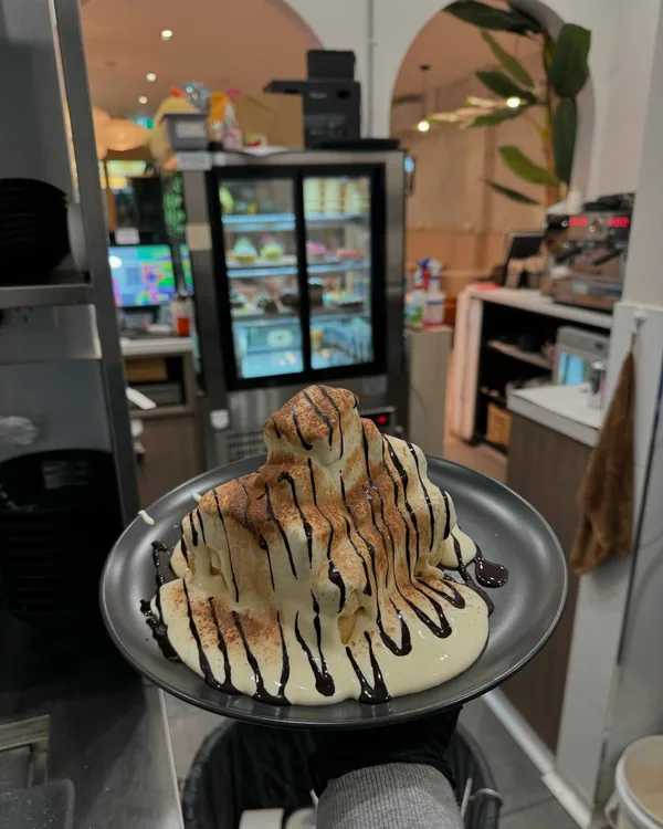 A bingsu under white chocolate and a chocolate drizzle, carried out from the kitchen