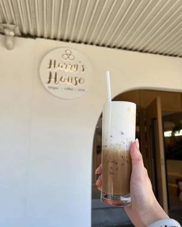 An iced coffee held up under our Harry's House sign