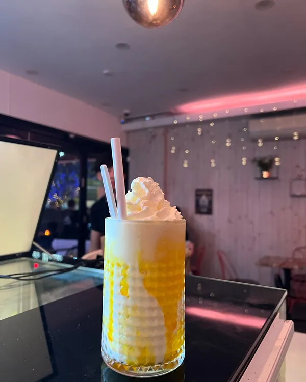 A tall yellow drink under whipped cream at the counter